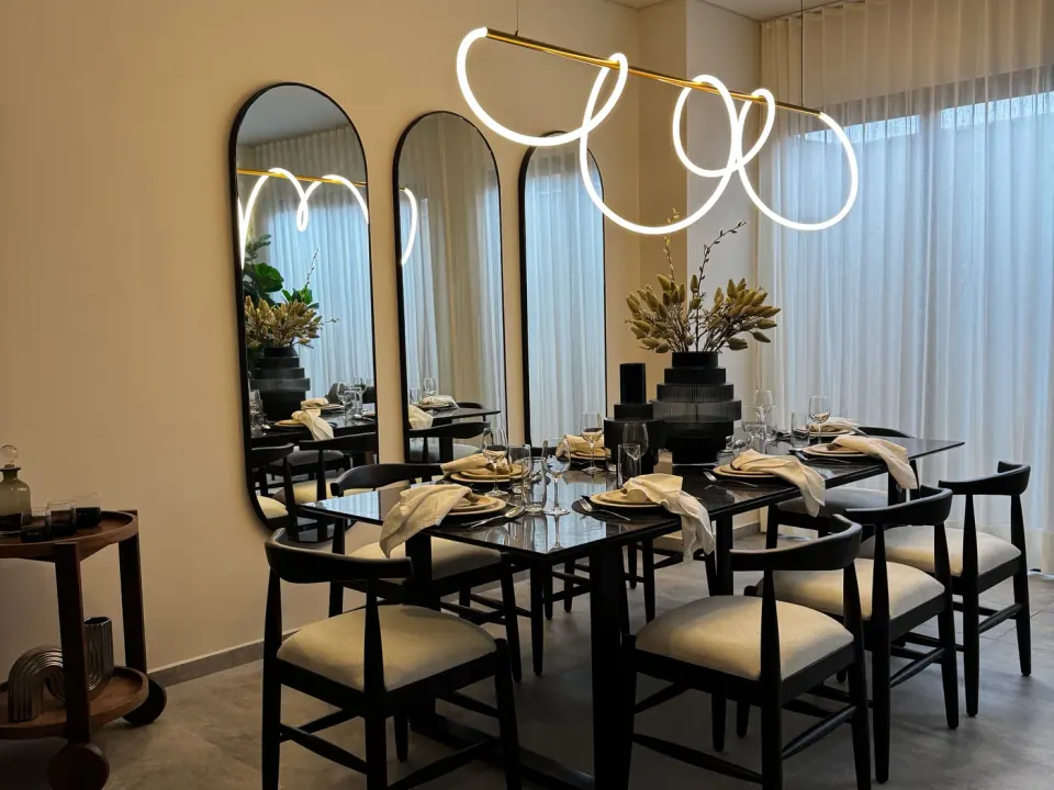 Comedor con mesa oscura, sillas negras de asiento claro y tres espejos de arco bajo una lámpara colgante luminosa