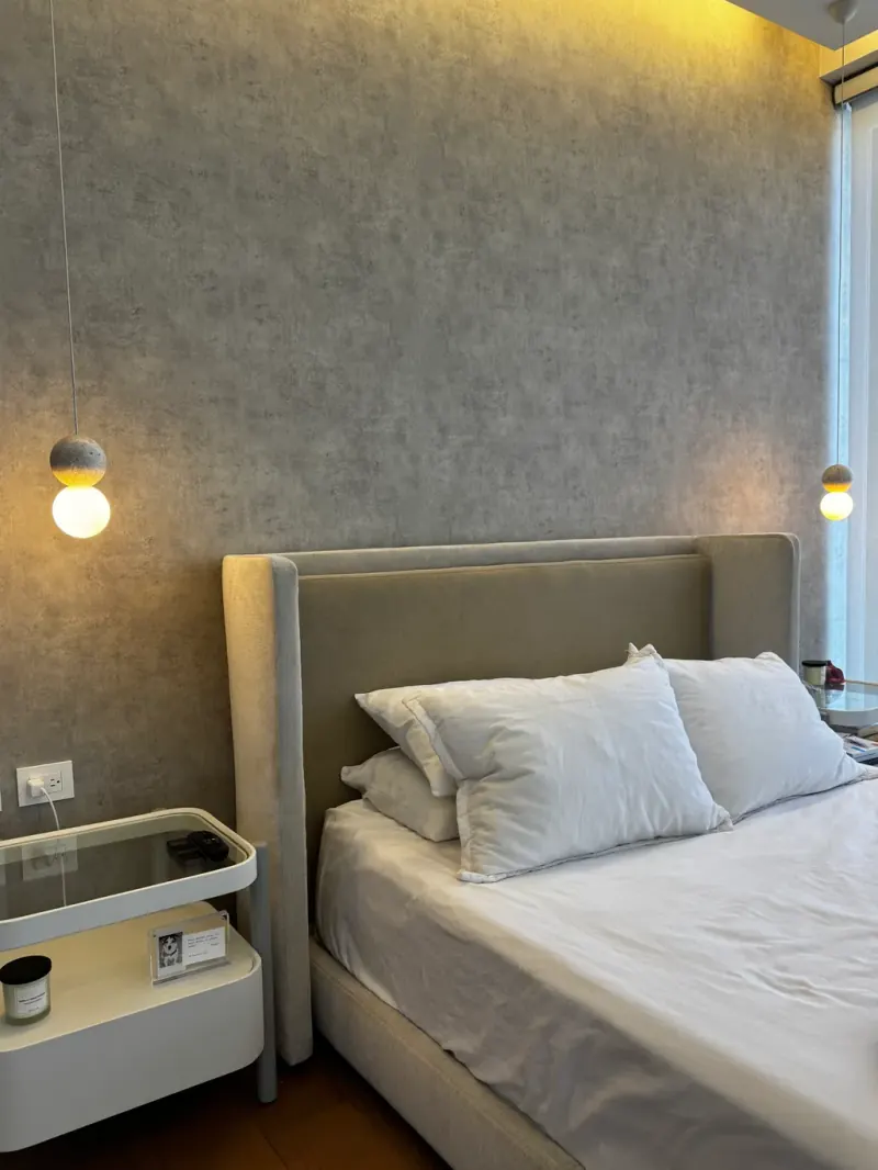 Cabecera beige con almohadas blancas, lámparas colgantes de esfera y pared gris de acabado texturizado
