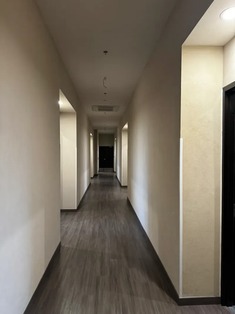 Pasillo largo de muros beige texturizados, vanos remetidos, piso oscuro y aire acondicionado en el plafón