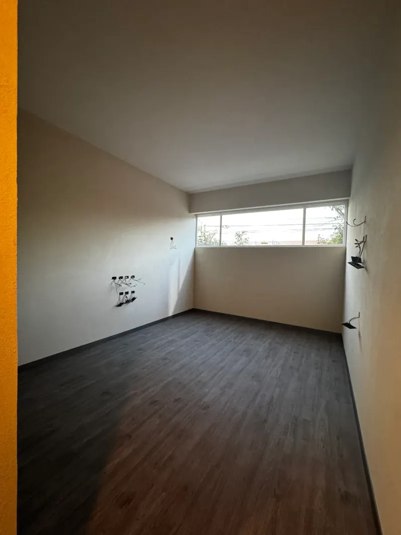Cuarto vacío con ventana alargada en lo alto del muro, piso oscuro y salidas eléctricas con cables a la vista
