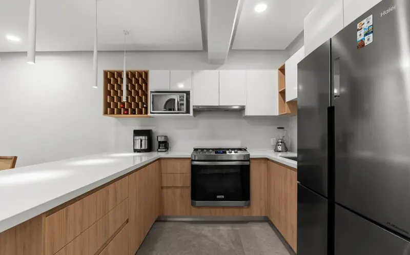 Cocina en forma de U con estufa, microondas y refrigerador, gabinetes bajos en tono madera y alacenas blancas