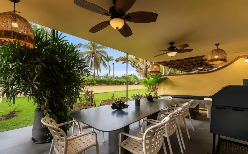 Terraza cubierta en Puerto Vallarta con mesa larga, sillas blancas, ventiladores de techo y palmeras al fondo