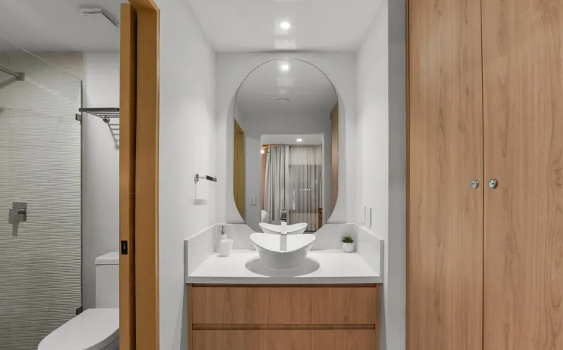 Baño con espejo de arco, lavabo sobrepuesto en mueble tono madera y regadera con muro de relieve ondulado