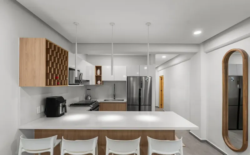 Barra de la cocina de frente con taburetes blancos, tres lámparas colgantes y un espejo alargado de marco de madera