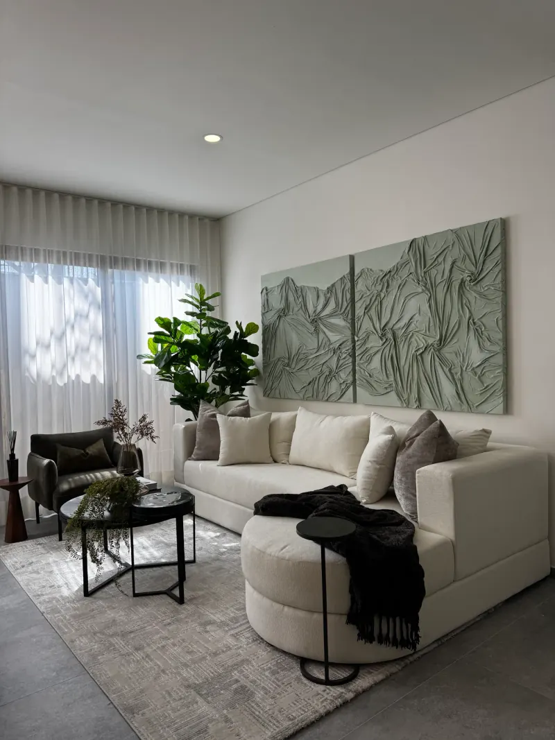 Sala con sofá crudo de chaise curva, panel texturizado en verde salvia, sillón oliva y dos mesas de centro negras