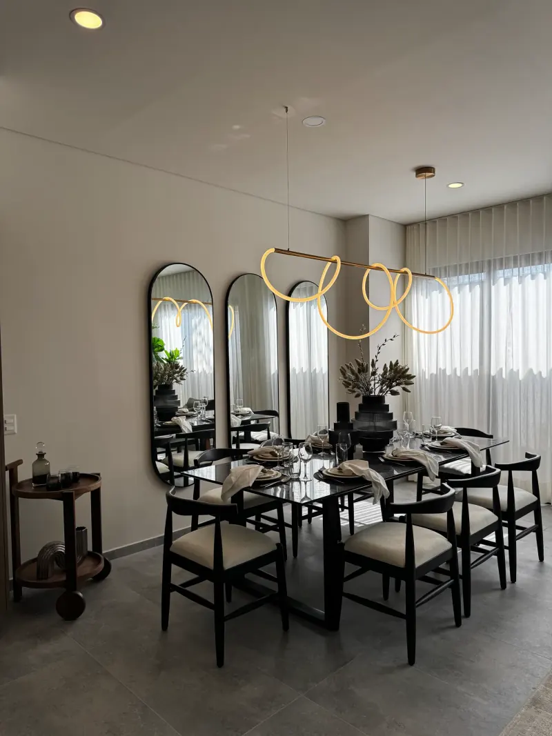 Comedor con la lámpara de tubo luminoso encendida, mesa servida y carrito auxiliar de madera junto al muro