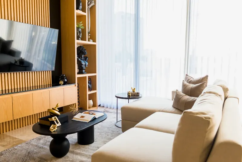 Muro de televisión con lamas verticales de madera clara y repisas con bustos negros junto a un sofá seccional