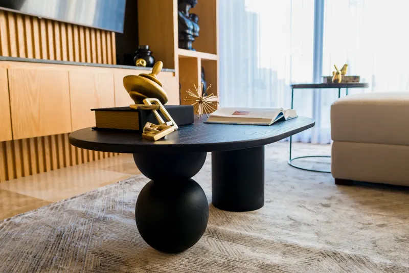 Mesa de centro negra con base de esfera y cilindro, objetos dorados y libros sobre un tapete gris