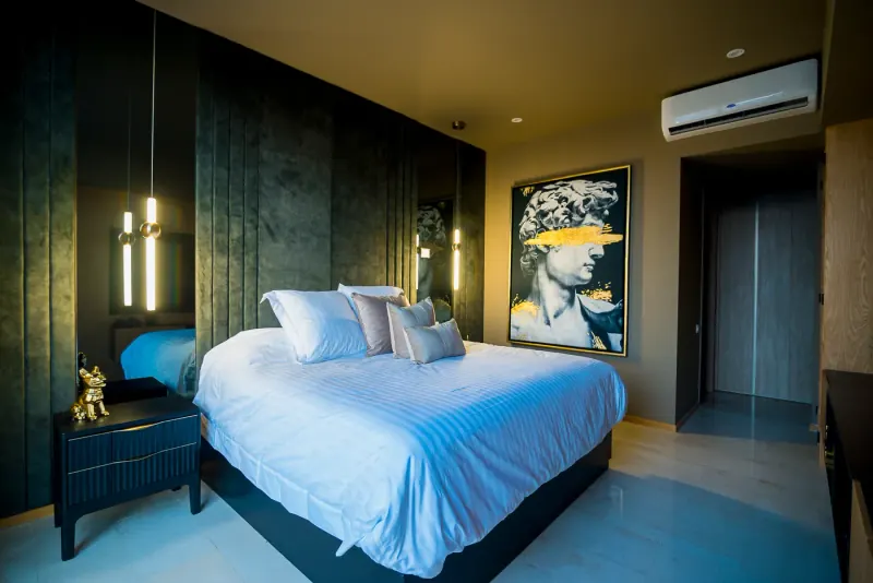 Recámara del Departamento DC con ropa de cama blanca, muro tapizado en verde oscuro y cuadro con busto clásico