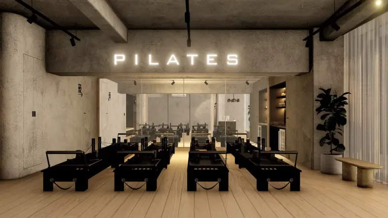 Letrero luminoso con la palabra PILATES sobre un faldón de acabado tipo concreto, con reformers negros al frente