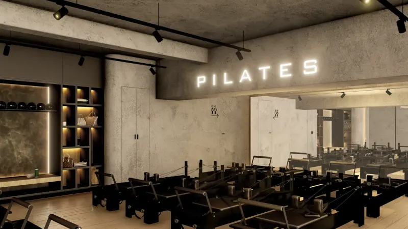 Vista diagonal con el letrero PILATES, el mueble de nichos y los reformers frente a una pared de cristal